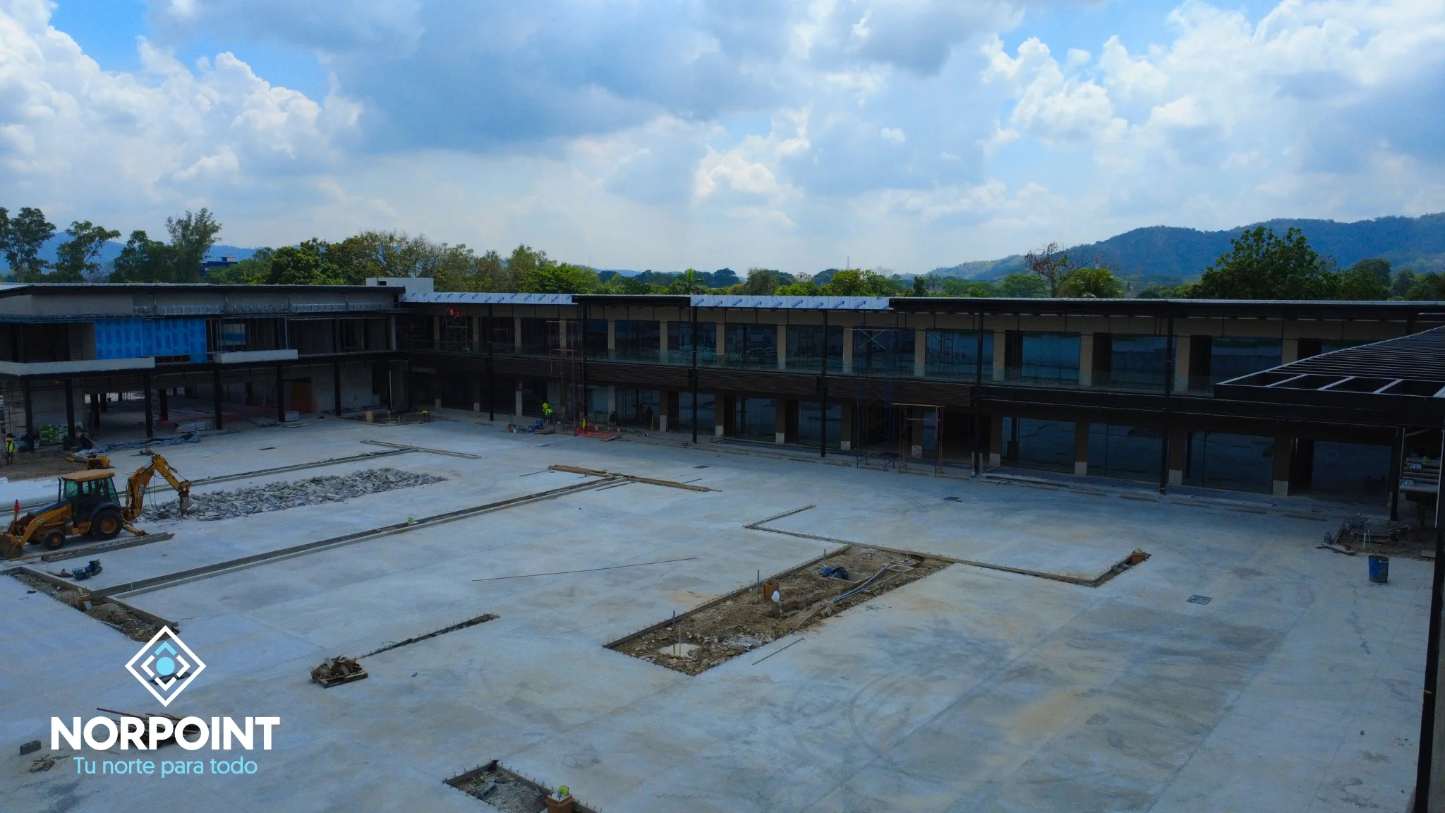Avance de junio en Norpoint con estacionamientocentral en construcción, módulos comerciales alrededor y progreso estructural del proyecto.